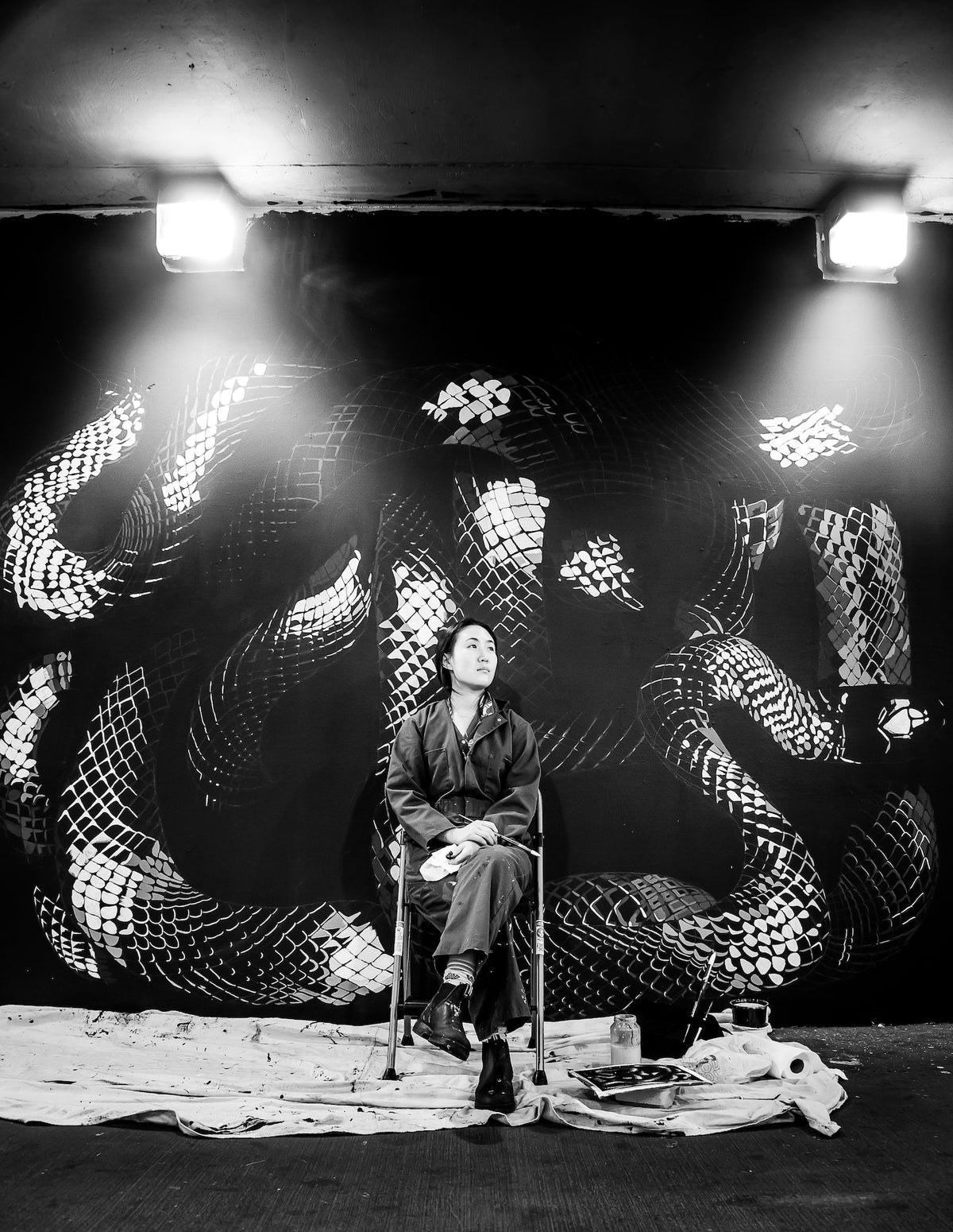 Black and white photo of artist sitting in front of a dragon mural